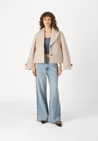 Ανοιχτό μπεζ cropped σακάκι με V-λαιμό, που διαθέτει δύο κουμπιά, συνδυασμένο με τζιν σε άνοιξη ψηλή μέση και καμπάνα και μαύρες μπαλαρίνες.