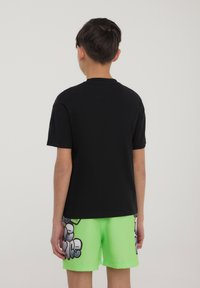 T-shirt nera a maniche corte con scollo rotondo, abbinata a pantaloni da bagno corti di un brillante verde neon con stampa grafica e dettagli bianchi.
