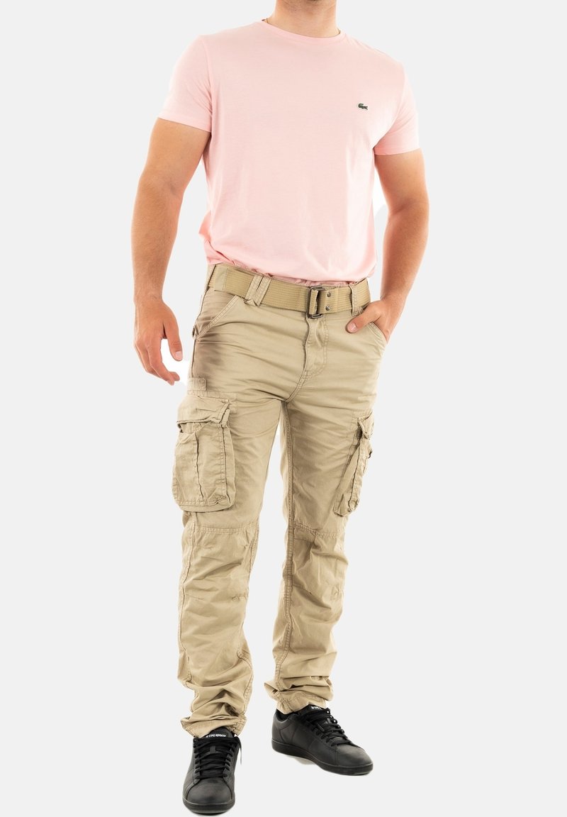 Beige cargobroeken met meerdere zakken, gecombineerd met een lichtroze katoenen t-shirt. Draagt zwarte schoenen, wat een casual, slimfit stijl laat zien.