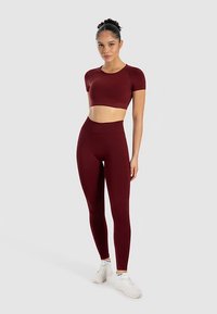 Bordeauxrød atletisk crop top og højttaljede leggings, lavet af glat stof, tætsiddende design, sømløs konstruktion med en diskret glans.