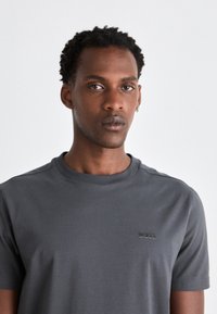 Grå polyester T-shirt med rund halsudskæring og korte ærmer. Har et diskret sort "BOSS" logo på brystet. Glat tekstur.