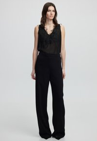 Top negro sin mangas con ribete de encaje y escote en V profundo, combinado con pantalones negros de cintura alta y perneras anchas en una tela suave.