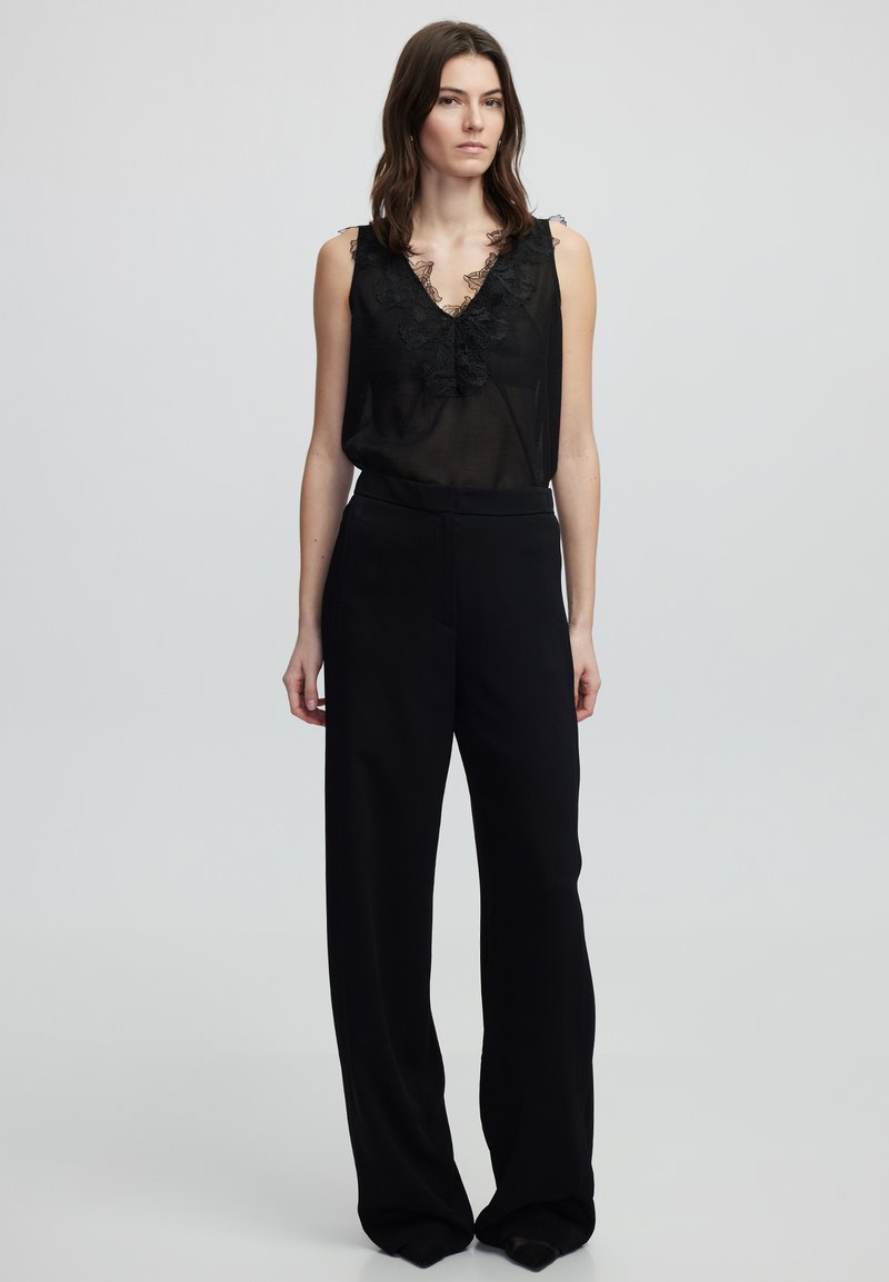 Top negro sin mangas con ribete de encaje y escote en V profundo, combinado con pantalones negros de cintura alta y perneras anchas en una tela suave.