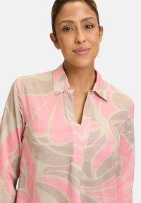 Langärmlige Bluse aus leichtem Stoff mit einem großen rosa-beigen abstrakten Blumenmuster, V-Ausschnitt und Kragen-Detail.