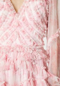 Abito rosa realizzato in tessuto stratificato e arricciato. Presenta una scollatura a V e lunghe maniche trasparenti con un delicato motivo floreale.