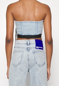 Nainen, jolla on päällään vaaleansininen happopesuinen farkkotuubipaita ja siihen sopivat korkeavyötäröiset farkut, joissa on takana sininen Karl Lagerfeld Jeans -label.