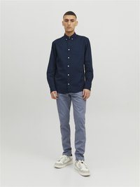 Marineblaues Hemd mit Knopfleiste, Kragen und Tasche, kombiniert mit hellgrauen Hosen und weißen Sneakers. Glattes Material mit lässiger Passform.
