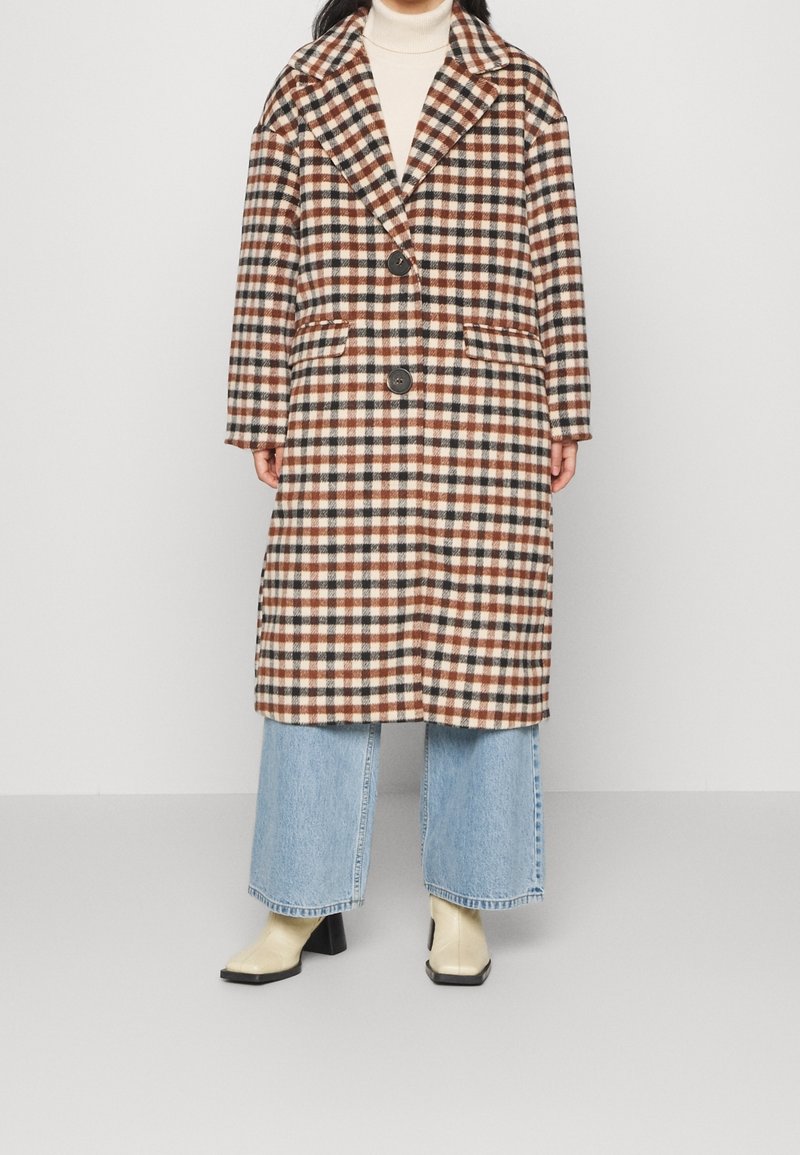 Karierte Jacke in Braun-, Cremewhite- und Rosttönen mit einem Reverskragen, zwei Knöpfen und seitlichen Taschen. Getragen über weit geschnittenen Jeans.