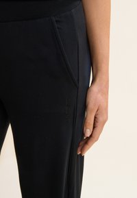 Pantalons de sport noirs avec poches latérales et détail de logo texturé. Fabriqués en matériau doux et extensible avec une coupe ajustée.
