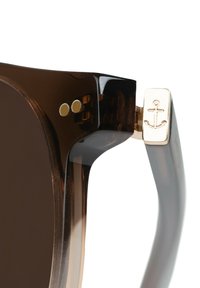 Braune Sonnenbrille mit transparenten Schildpatt-Frames. Verfügt über ein goldenes Ankeremblem am Bügel und metallische Akzente.