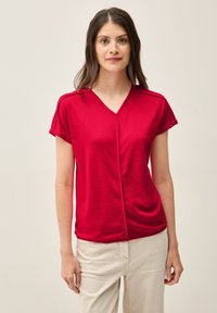 Top rojo de manga corta con escote en V, que presenta mangas enrolladas y un cuerpo ligeramente drapeado. Fabricado con un tejido ligero y texturizado.