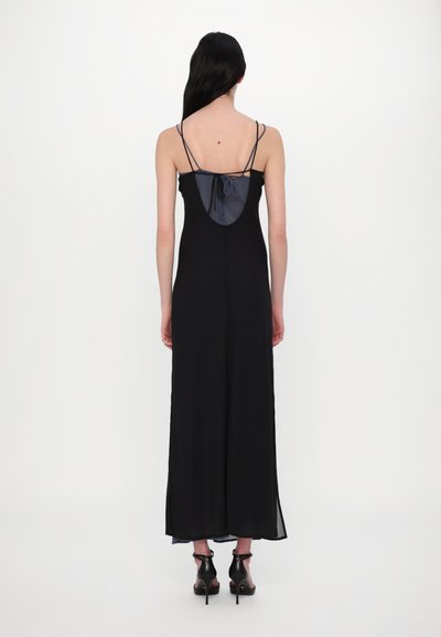 Rochie neagră cu bretele subțiri, un panou dintr-un material transparent la spate și un detaliu legat. Are un design lung până la podea și o strălucire subtilă.