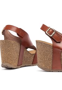 Brown leather wedge sandals with cork platform, adjustable ankle strap, and open-toe design, featuring a textured finish and contrasting accents.
