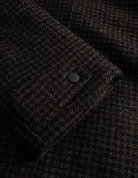 Καφέ καρό ύφασμα με υφαντή επιφάνεια, διαθέτοντας λεπτομέρεια με μαύρο κουμπί πατήματος σε διπλωμένη άκρη.