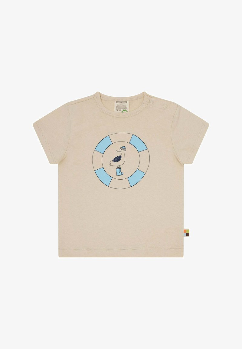 Hellbeige T-Shirt mit kurzen Ärmeln, das ein rundes blau-weißes Logo mit einem Pelikan in Hut und Stiefeln zeigt, aus weicher Baumwolle gefertigt.