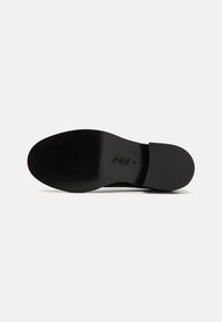 Black shoe sole with a smooth finish. Features a rounded shape and engraved logo design. Minimal texture and no visible hardware.