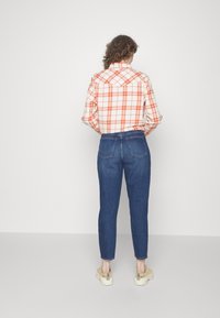 Camisa de cuadros roja y blanca de manga larga, combinada con unos jeans ajustados azul oscuro. Cuenta con un cuello abotonado y bolsillos traseros. Se lleva con zapatillas beige.