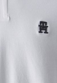 Polo bianco in tessuto testurizzato, con logo ricamato blu navy sul lato sinistro del petto. Collo classico e dettagli della patta con bottoni.