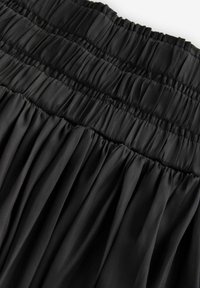 Schwarzer plissierter Rock aus glattem Stoff mit geraffter Textur, ausgestattet mit einem elastischen Bund und fließendem Design.