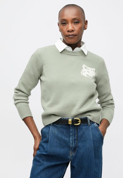 Suéter de punto verde claro con cuello redondo y mangas largas, que presenta un diseño de un zorro blanco en el pecho, combinado con unos pantalones vaqueros azules de cintura alta.