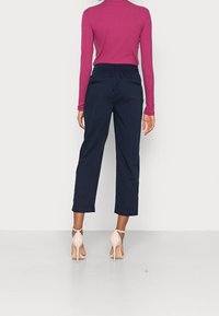 Pantalones cortos de color azul marino con una cintura elástica y bolsillos traseros, combinados con una blusa de manga larga magenta y tacones en color nude.