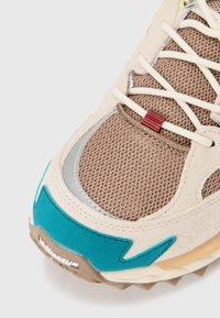 Brązowe siatkowe sneakersy z turkusowymi akcentami, szarymi metalicznymi detalami oraz beżowymi zamszowymi nakładkami. Posiadają białe sznurówki i teksturowaną beżową podeszwę.
