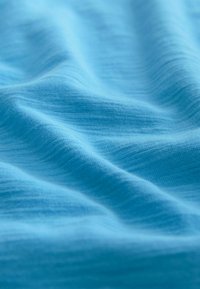 Helles blaues Gewebe mit einer weichen, strukturierten Oberfläche, die subtile Wellen aufweist und eine leichte, atmungsaktive Qualität besitzt.