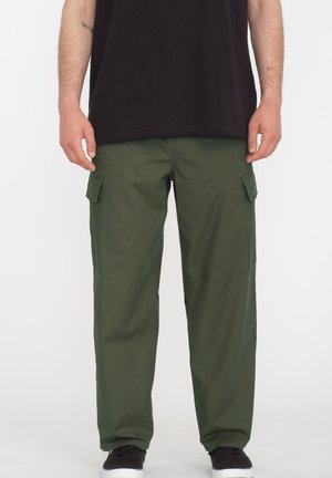 Pantaloni cargo in tessuto di cotone verde scuro, con due tasche laterali, una vestibilità relax e una texture complessiva liscia. Abbinati a una maglietta nera.