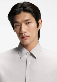 Vaaleanharmaa napillinen paita raidallisella kuviolla, jossa on terävä kaulus ja valkoiset napit, sileä pinta.