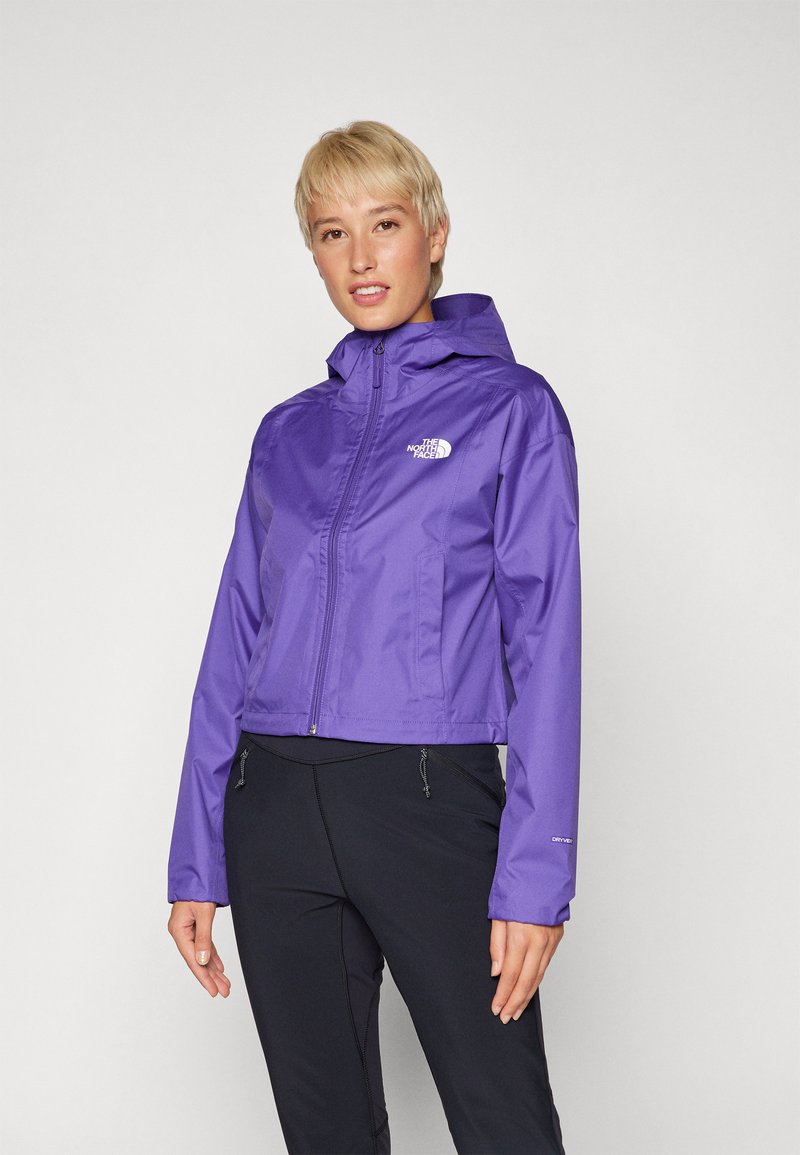 Giacca impermeabile viola con cappuccio, zip completa e logo sul petto. Presenta polsini elastici e un design cropped.