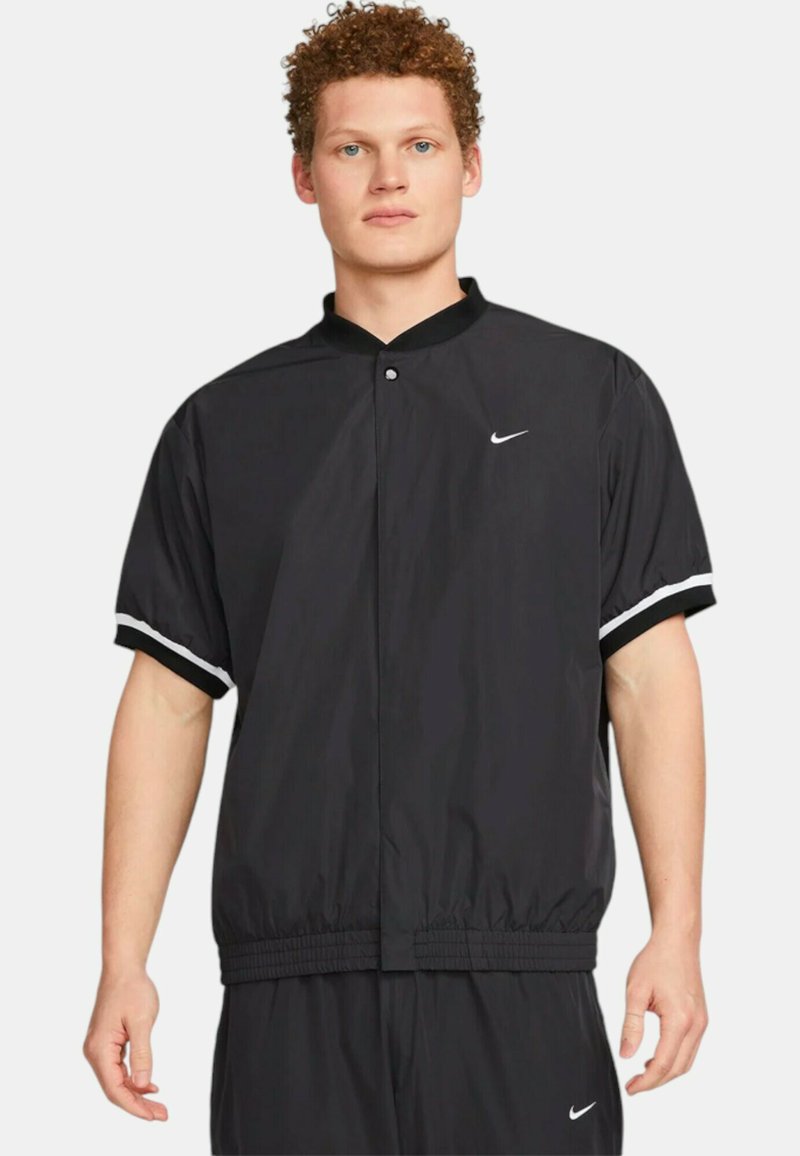 Giacca a vento nera con maniche corte, fascia elastica in vita e strisce bianche sui polsini. Caratterizzata da una chiusura con bottone e dal logo Nike.