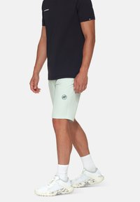 Lys mintgrønne shorts med et logo-patch, parret med en sort t-shirt. Modellen bærer hvide træningssko og ankelsokker i hvid.