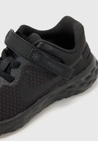 Chaussure de sport noire avec une tige en maille, sangle Velcro et semelle en caoutchouc dotée d'un motif texturé. Le design favorise une mise en chaussure facile.