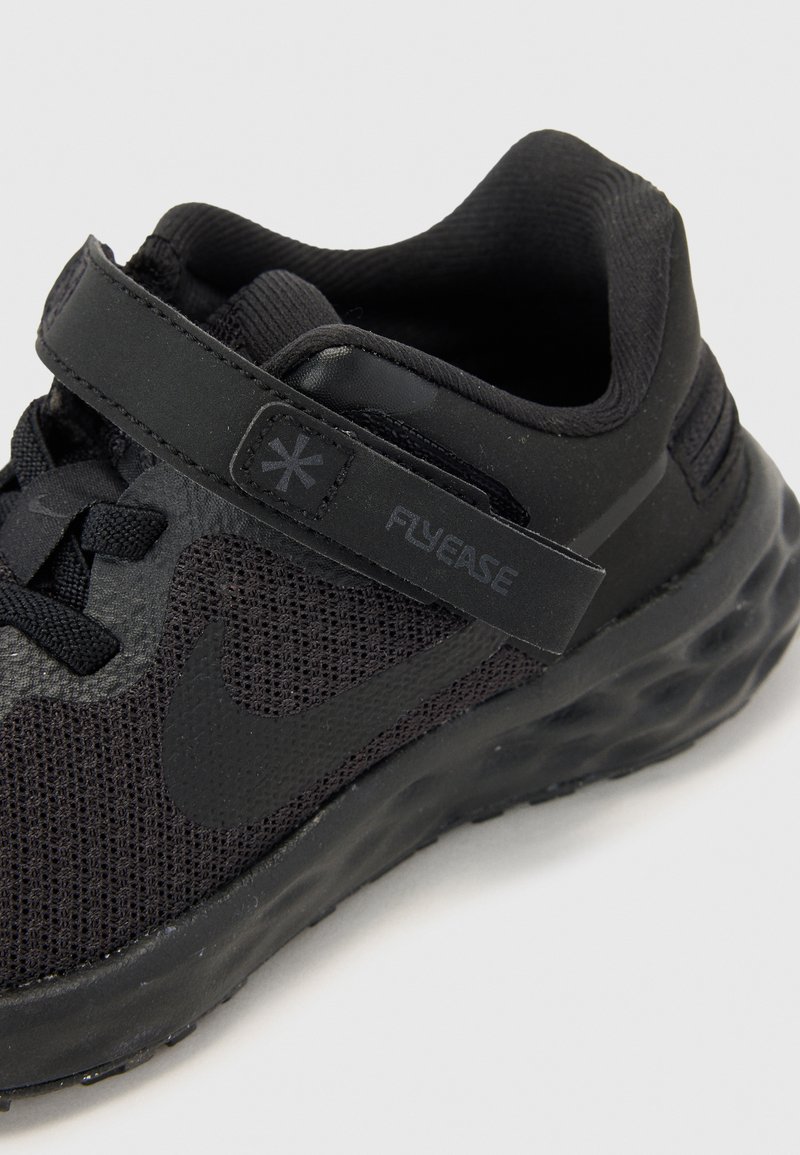 Scarpa sportiva nera con tomaia in rete, cinturino in velcro e suola in gomma con un motivo testurizzato. Il design agevola l'indossabilità.