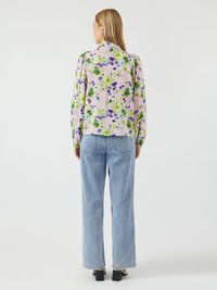 Blusa floral em rosa com flores verdes e roxas, com mangas bufantes e colarinho, combinada com jeans de cintura alta em azul claro.