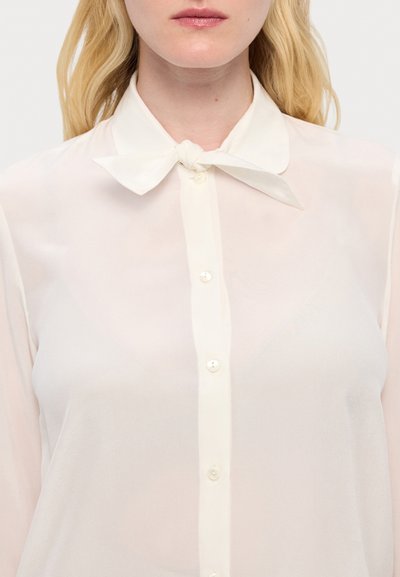 Leichte, durchsichtige Bluse in hellem Creme mit Kragen und Schleifendetail. Verfügt über Perlenknöpfe entlang der Vorderseite und hat eine glatte Textur.