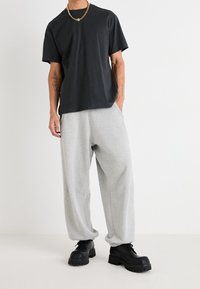 Schwarzes Baumwoll-T-Shirt mit Rundhalsausschnitt, kombiniert mit hellgrauen, lässig geschnittenen Jogginghosen. Schwarze Boots mit dicker Sohle runden das Outfit ab.