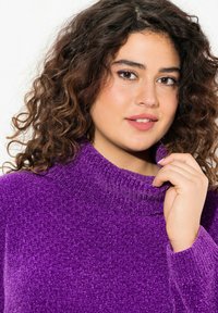 Lila, strukturerad, stickad tröja med hög, ribbad krage och långa ärmar. Tyget ser mjukt och något fluffigt ut.