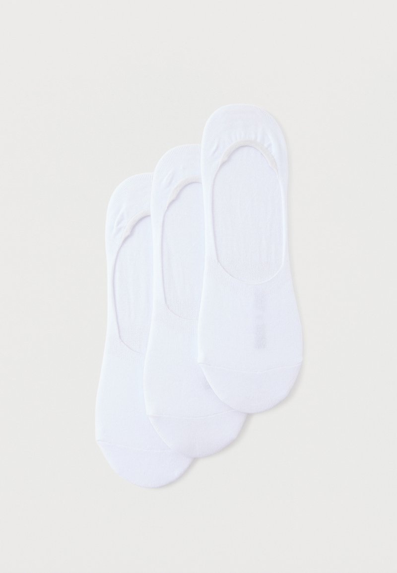 Trois paires de socquettes blanches unies disposées en chevauchement sur un fond clair.