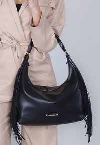 Borsa hobo in pelle nera con dettagli in frange, chiusura a zip e hardware dorato. Texture morbida e liscia con una forma morbida.