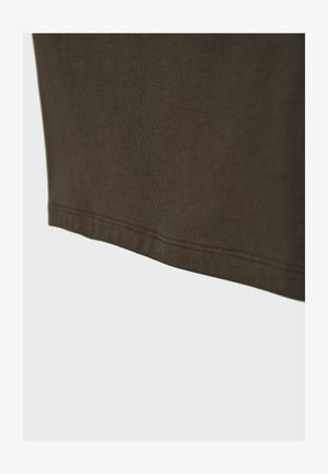 Zatamnjenozeleni tkanina izbliza prikazuje rub poruba sa ravnim šavom na glatkoj tkanini.