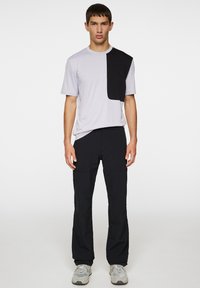 Jasnoszara koszulka z czarnym geometrycznym wzorem, zestawiona z czarnymi spodniami. Stylizacja ma luźny krój i teksturowane materiały.