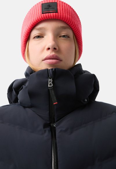 Schwarze Pufferjacke mit hohem Kragen und Reißverschluss, kombiniert mit einer leuchtend rosa gerippten Strickmütze mit einem schwarzen Logo-Patch.