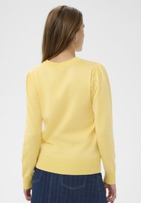 Pull en tricot jaune avec ourlet et poignets côtelés, manches bouffantes et encolure ronde, présenté de dos.