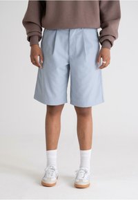 Light blue tailored shorts with pleats, featuring a relaxed fit, side pockets, and a soft, smooth texture. Worn with white socks and sneakers.