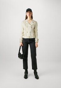 Veste de motard en cuir couleur crème avec un devant croisé, une ceinture et des accessoires en métal argenté. Un jean noir et des bottines complètent la tenue.