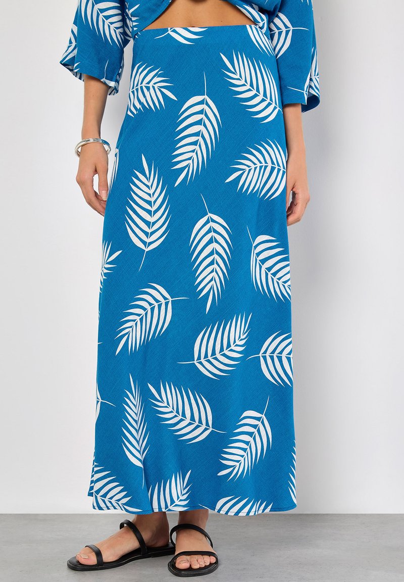 Maxi-Rock aus blauer Stoff mit einer strukturierten Oberfläche. Mit weißen Blattformen verziert. Kombiniert mit schwarzen flachen Sandalen und einem silbernen Armreif.