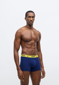 Tmavomodré boxerky s žltým pásikom Nike a logom, vyrobené z hladkého, pružného materiálu pre pohodlie a podporu.