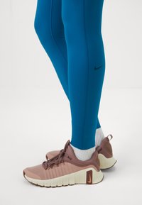 Tirkizne tajice s crnim Nike logotipom, uparene s smeškim i kremastim Nike tenisicama s bijelim vezicama i teksturiranom potplatom.