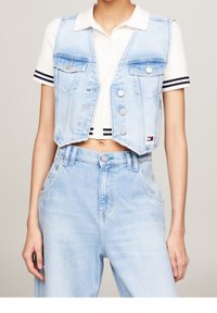 Ljusblå denimcroppad väst med fyra framfickor och silverdetaljer, parat med en vit ribbad skjorta med marinblå ränder.